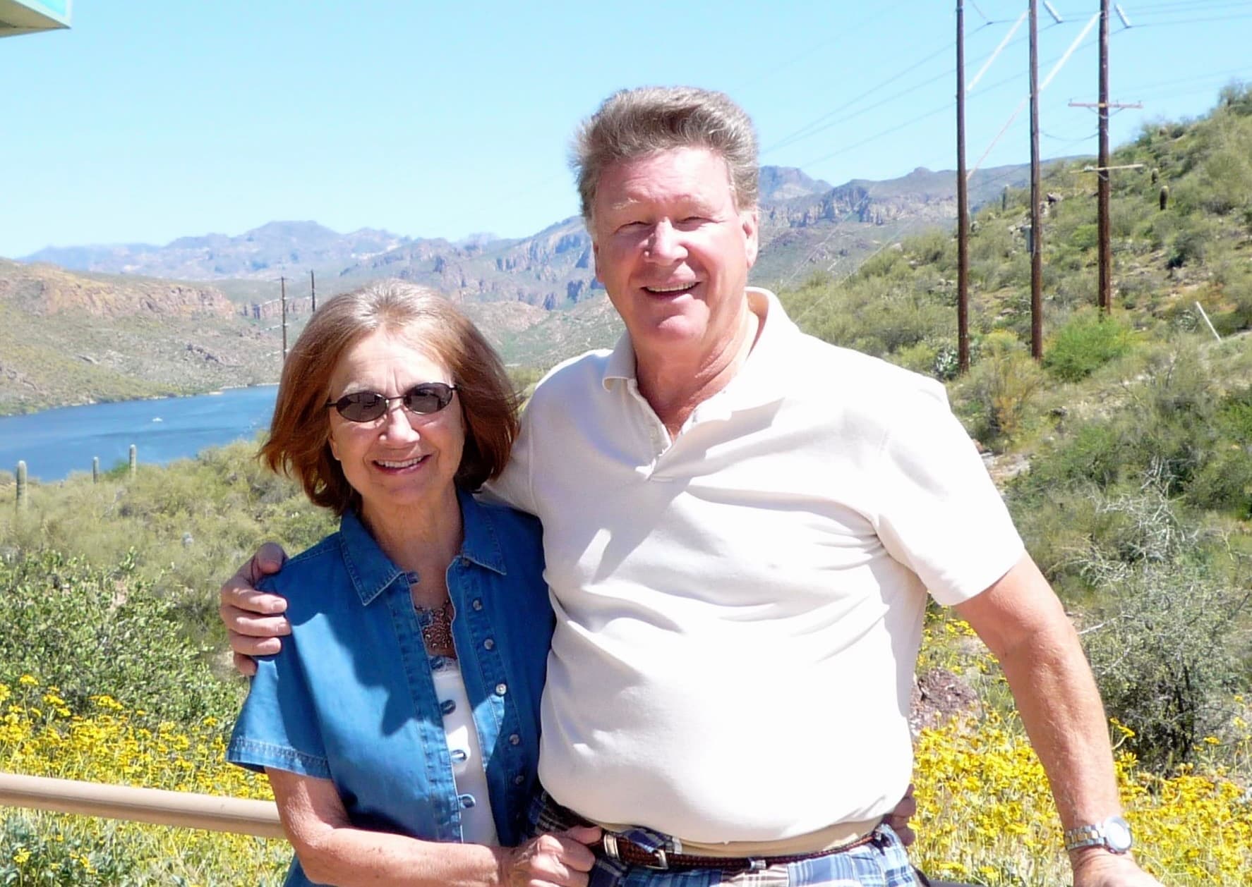 Wanda and a man standing together outdoors, a lake and desert hills behind them